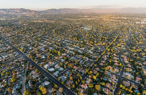 Aerial view of a sprawling suburban neighborhood with rows of houses and trees, under a golden sunset.