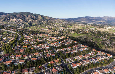 Aerial view of a residential neighborhood with houses and red roofs, in front of mountains under a blue sky.