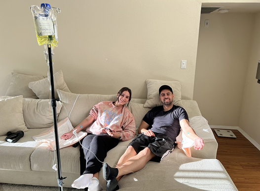 Two people on a couch receiving IV infusions in a home.