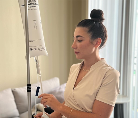 Woman in white scrubs, next to an IV drip stand, preparing the equipment.