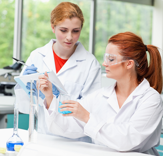 Two women in lab coats, one pouring liquid into a beaker, the other taking notes. Bright laboratory.
