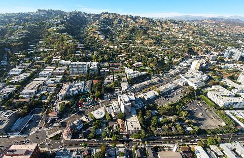 Aerial view of a residential and commercial area in a sunny environment with hills in the background.
