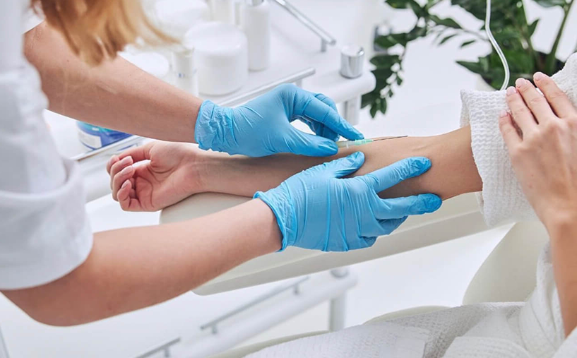 Person receiving IV infusion; healthcare worker in blue gloves preparing the arm.