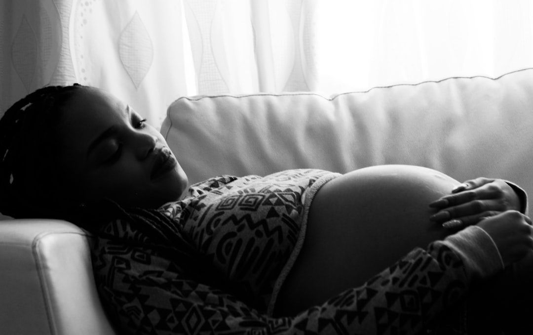 Pregnant woman resting on a couch, hands on her belly, eyes closed, soft light.