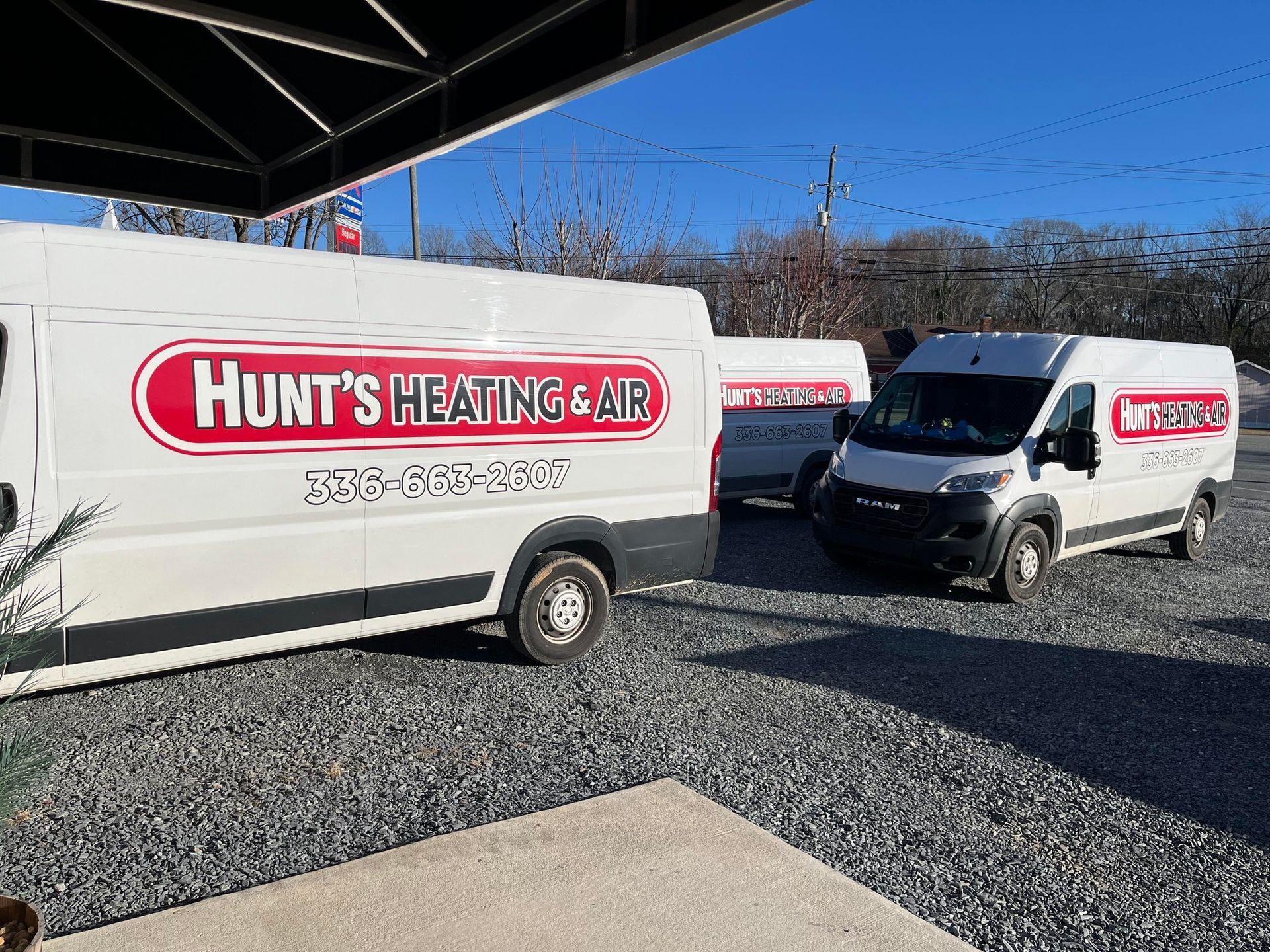Two white vans are parked next to each other in a gravel lot.
