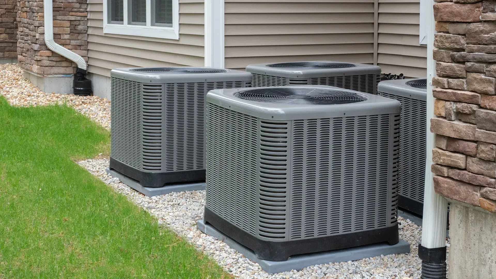 Three air conditioners are sitting outside of a house.