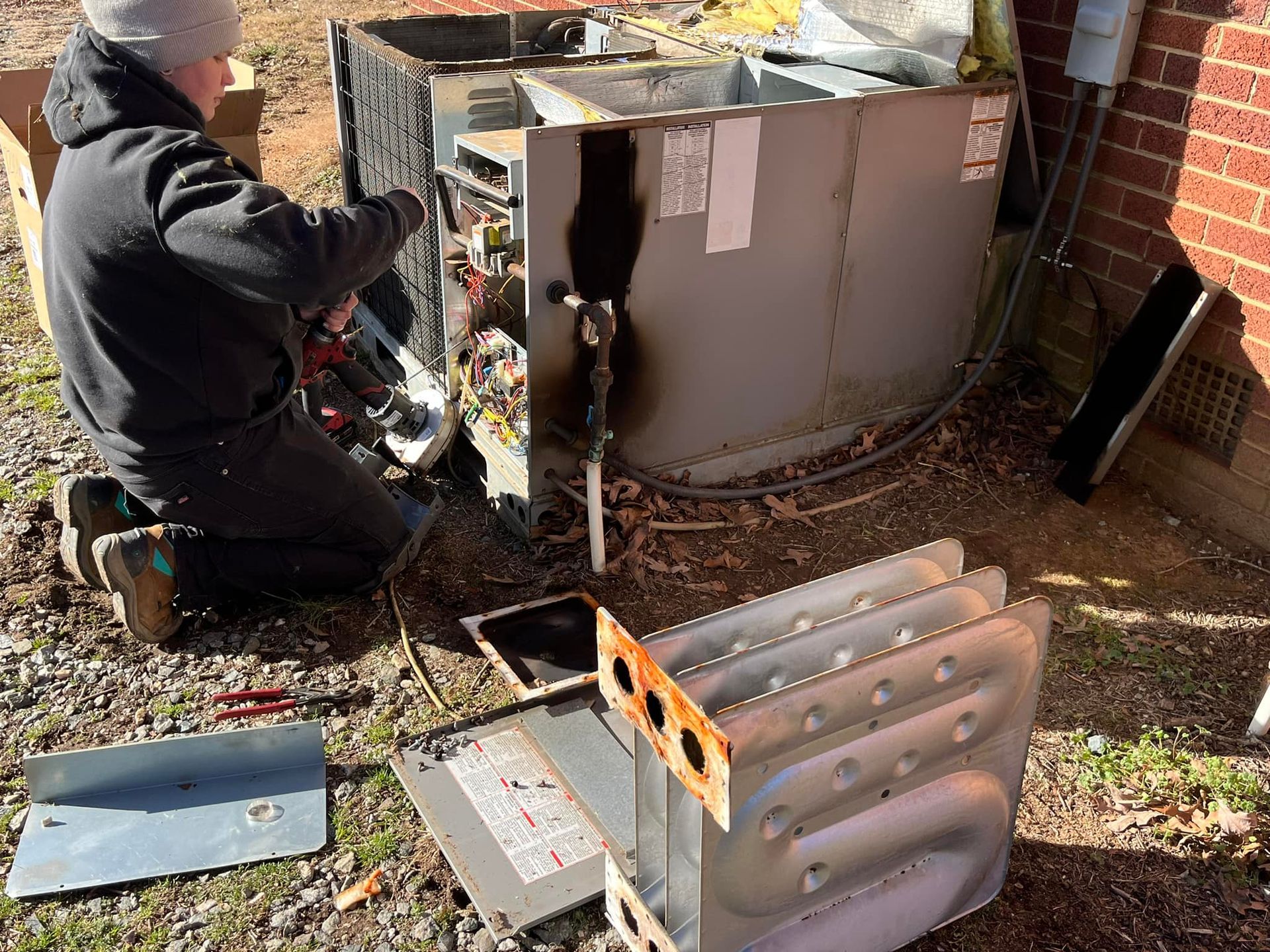 A man is working on an air conditioner outside of a brick building.