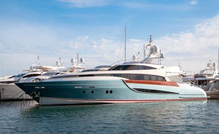 A sleek, teal and white luxury yacht docked in a marina under a bright blue sky.