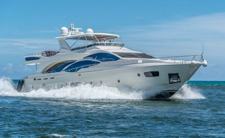 A white luxury motor yacht cruising at speed through blue ocean water under a clear sky.