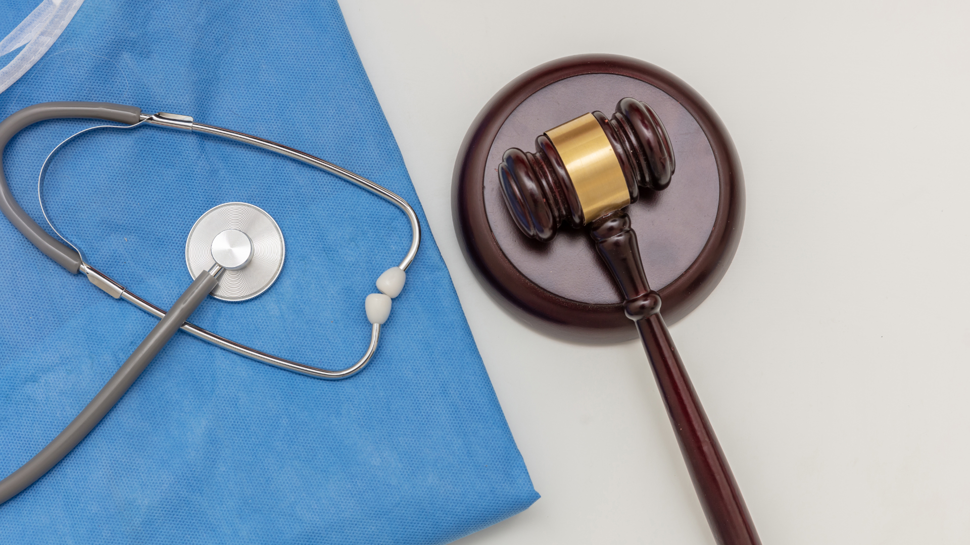 Stethoscope on blue surgical cloth next to a gavel on a wooden block, symbolizing medical law.