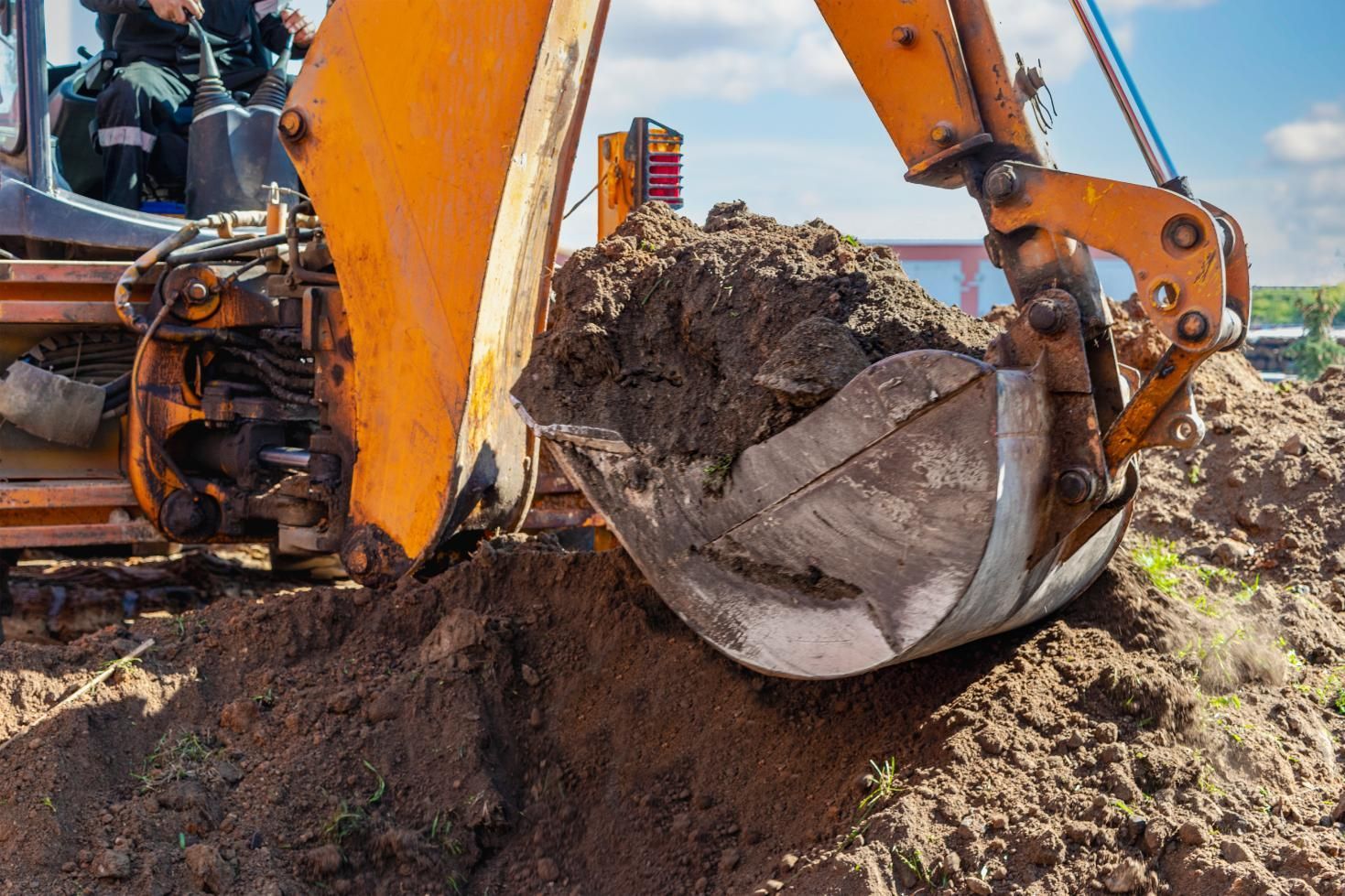 Excavator bucket scooping dirt at a construction site under a blue sky