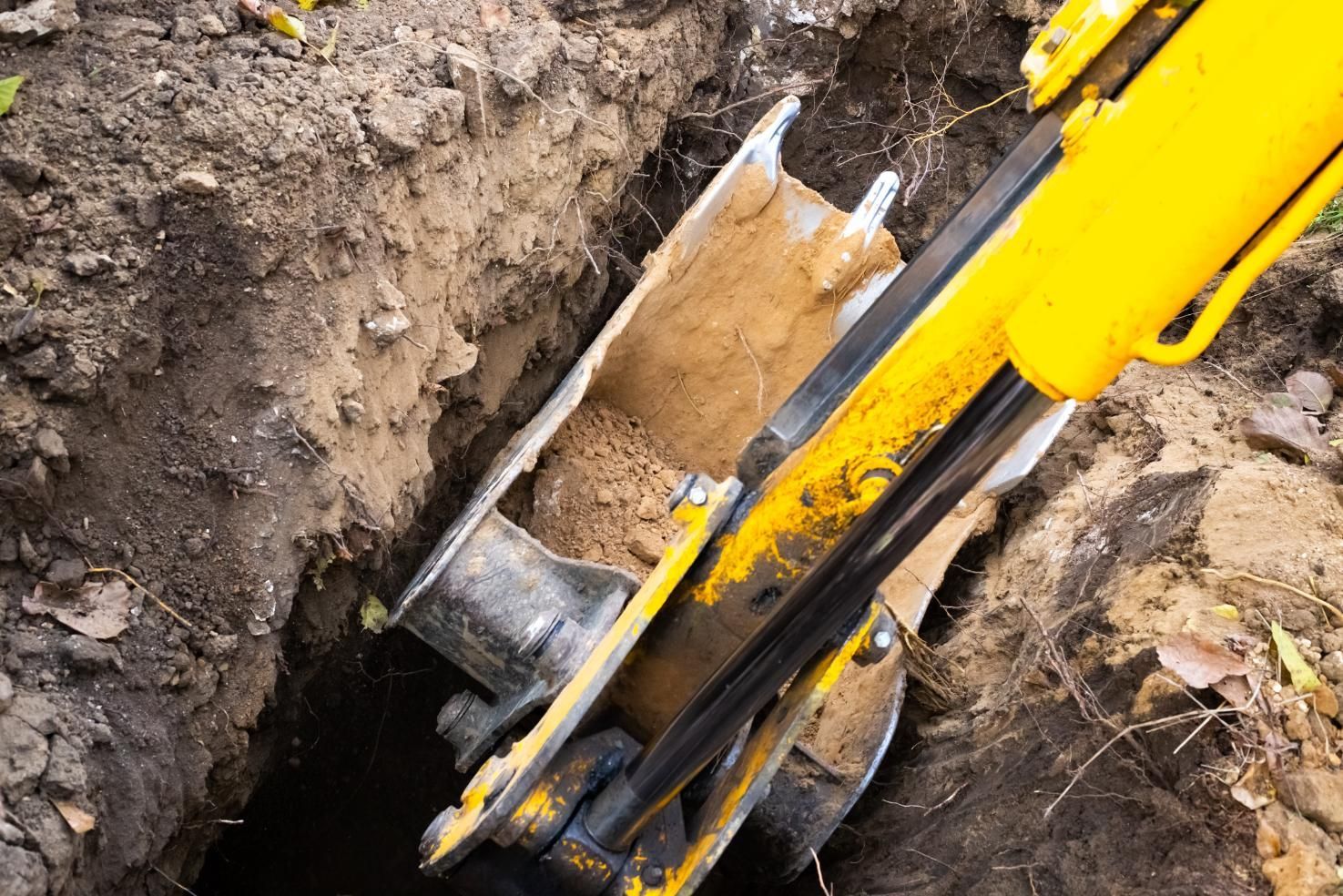 Yellow excavator bucket digging in muddy trench, close-up of earth and metal blade