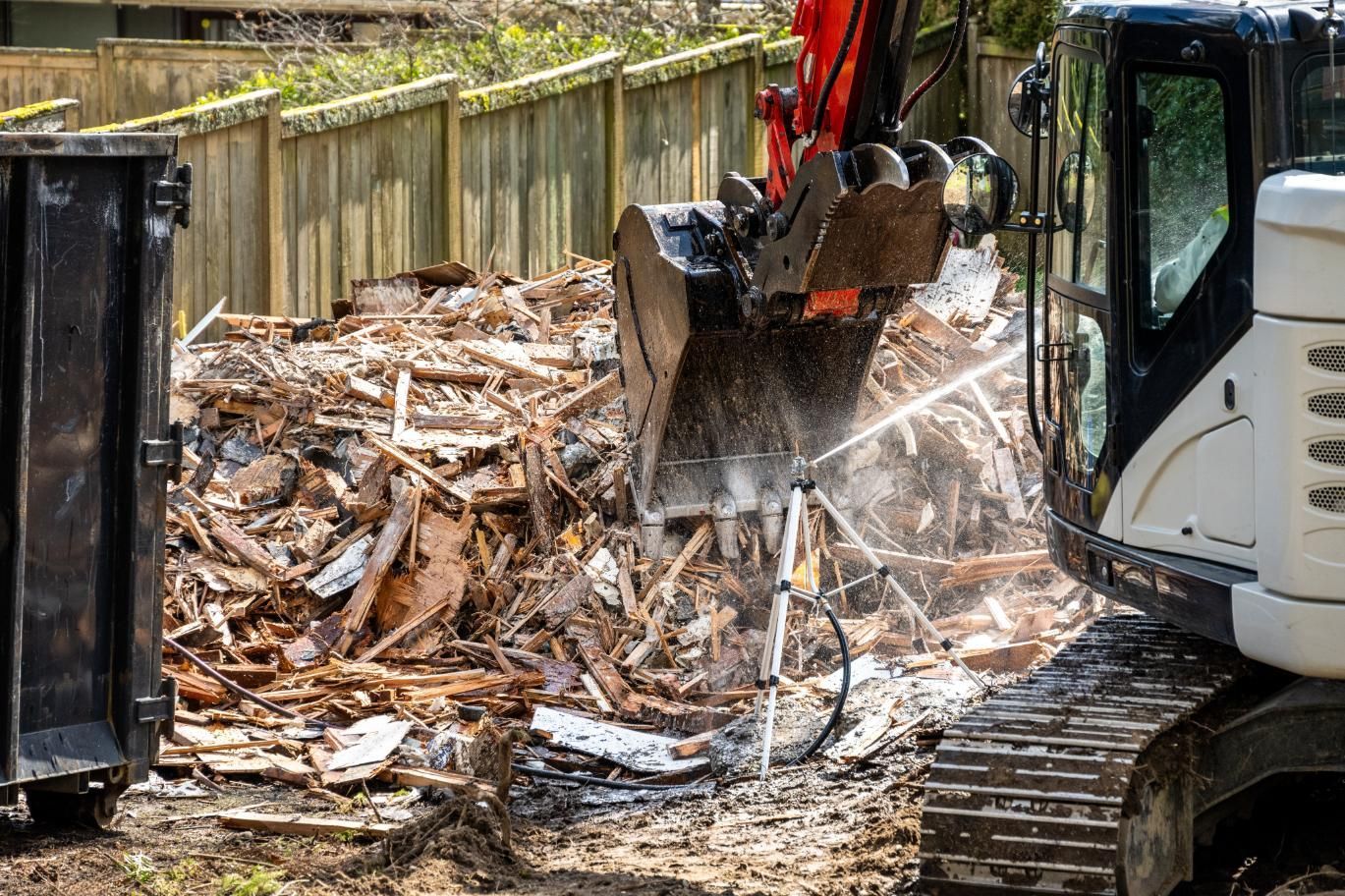 Excavator tearing down debris at a construction site beside a wooden fence.