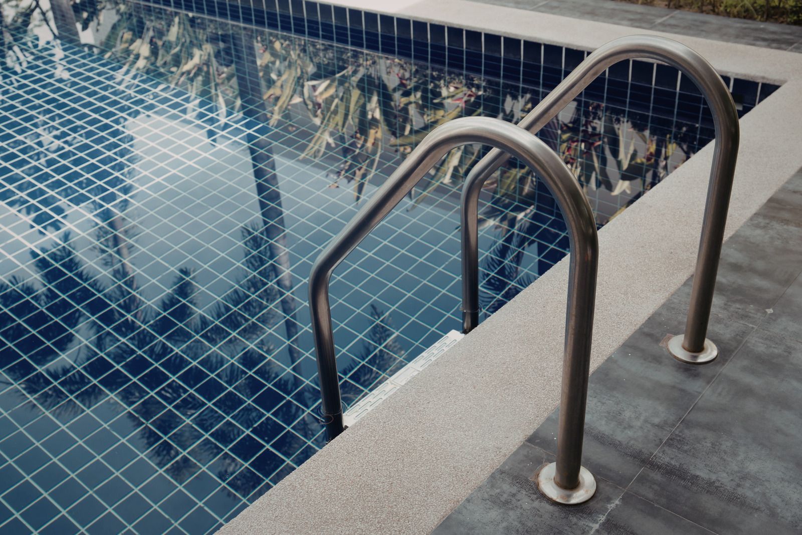 Stainless steel ladder leading into a swimming pool with dark blue square tiles.
