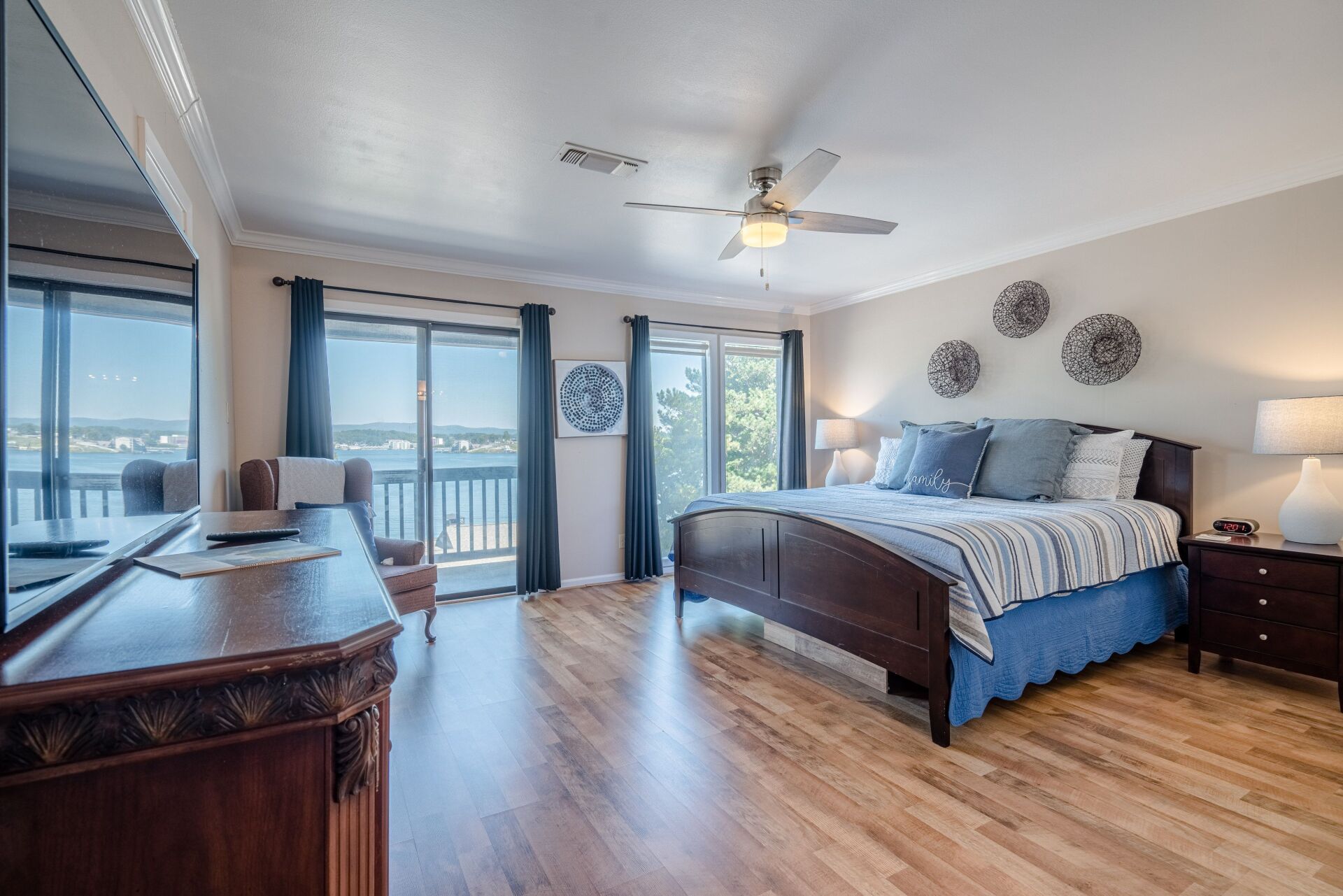 A large bedroom with a king size bed , a flat screen tv , a dresser and a balcony.