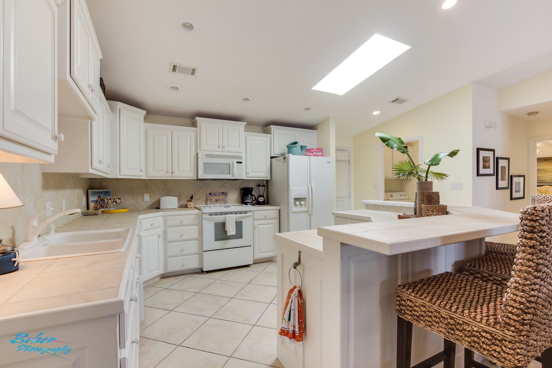 A kitchen with white cabinets , a stove , a refrigerator , a sink , and a bar.