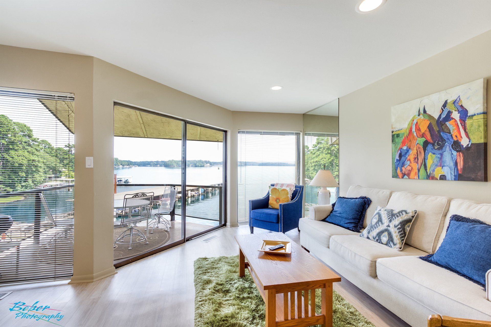 A living room with a couch , chair , coffee table and large windows overlooking a lake.