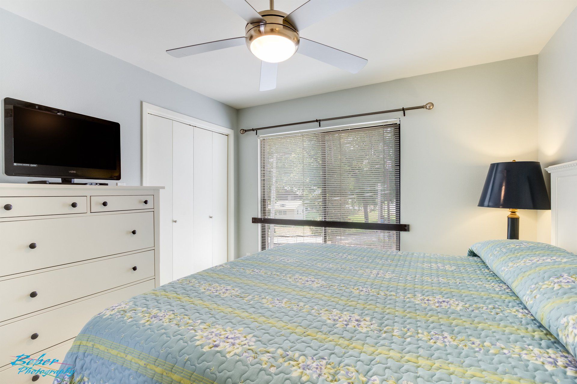A bedroom with a bed , dresser , television and ceiling fan.
