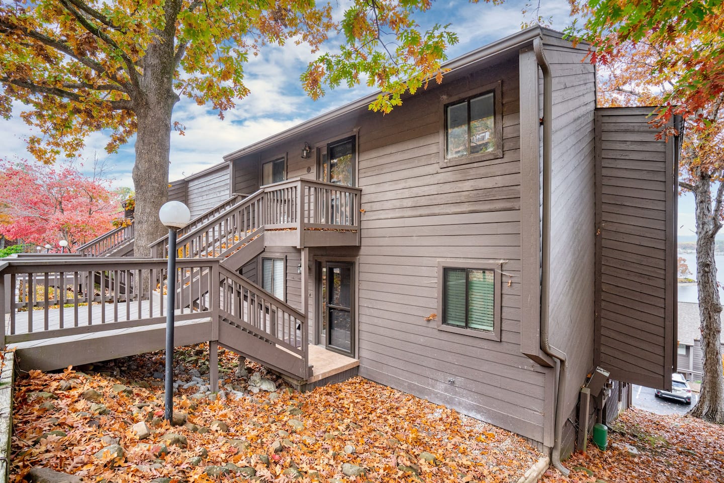 A house with a deck and stairs surrounded by trees and leaves.