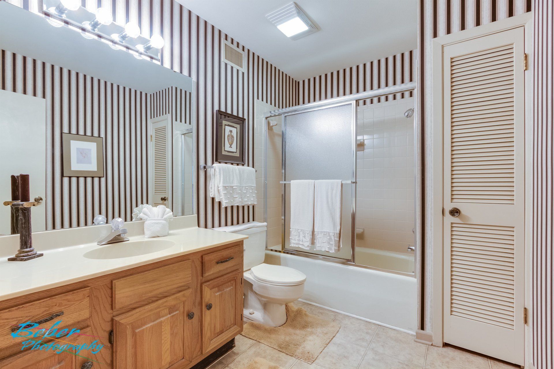 A bathroom with striped wallpaper , a sink , toilet , and bathtub.