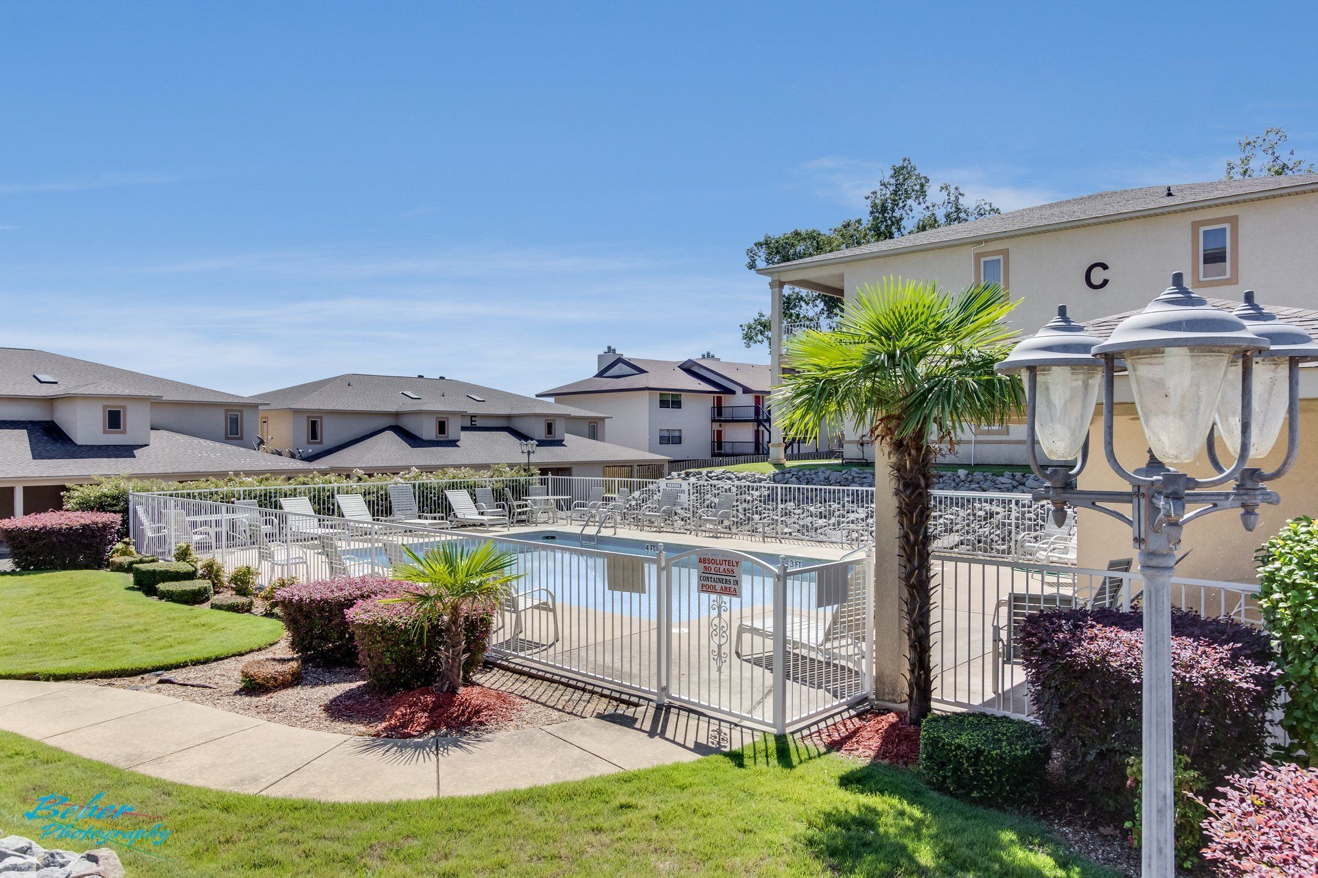 A large swimming pool is surrounded by a fence in front of a building with the letter c on it