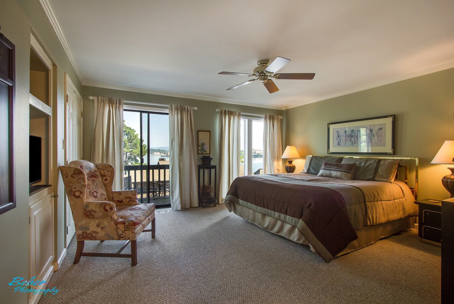 A bedroom with a large bed , chair , ceiling fan and sliding glass doors.