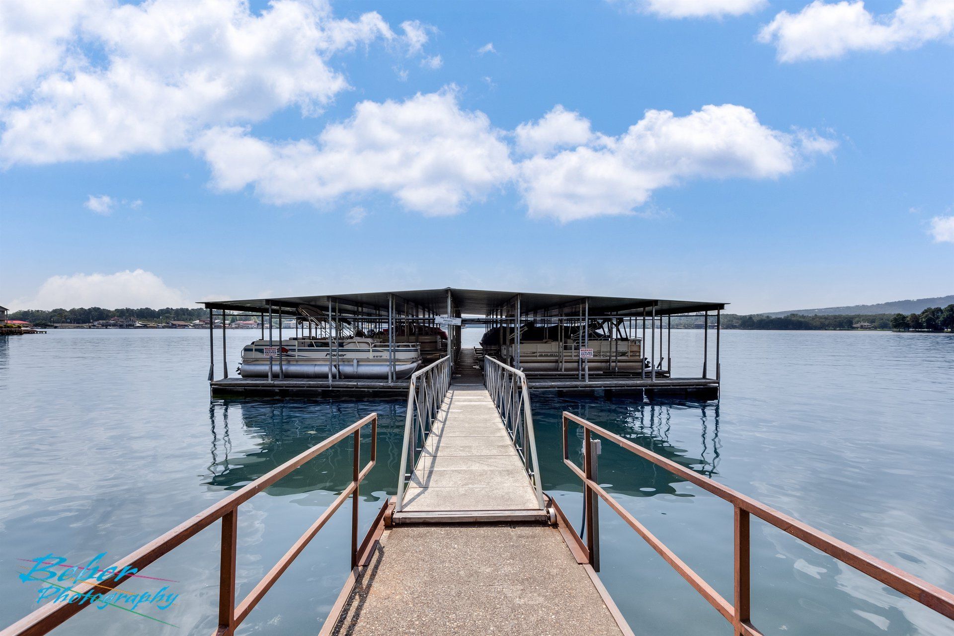 A dock with boats docked at the end of it on a lake.