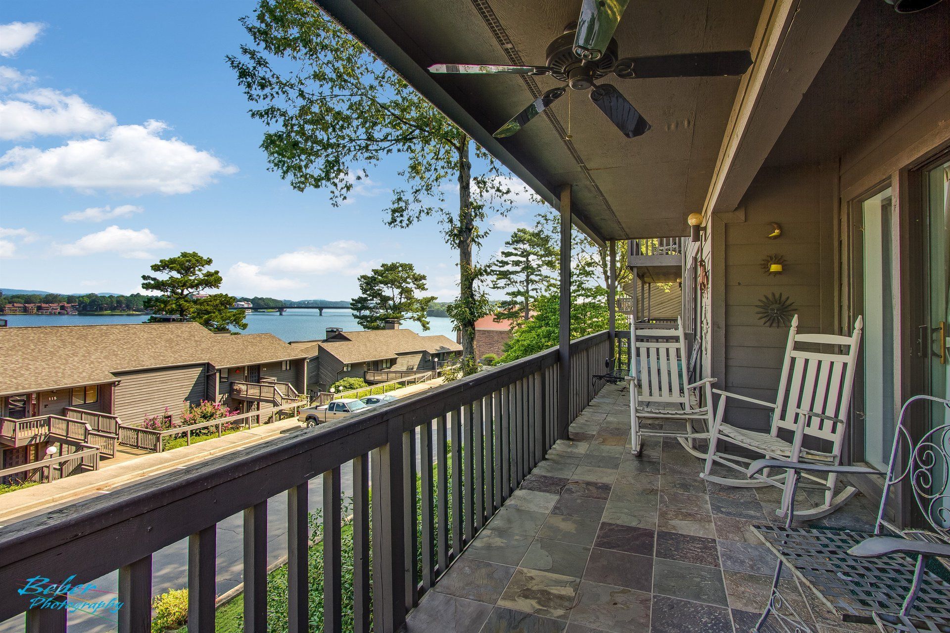 A balcony with rocking chairs and a ceiling fan overlooking a body of water.
