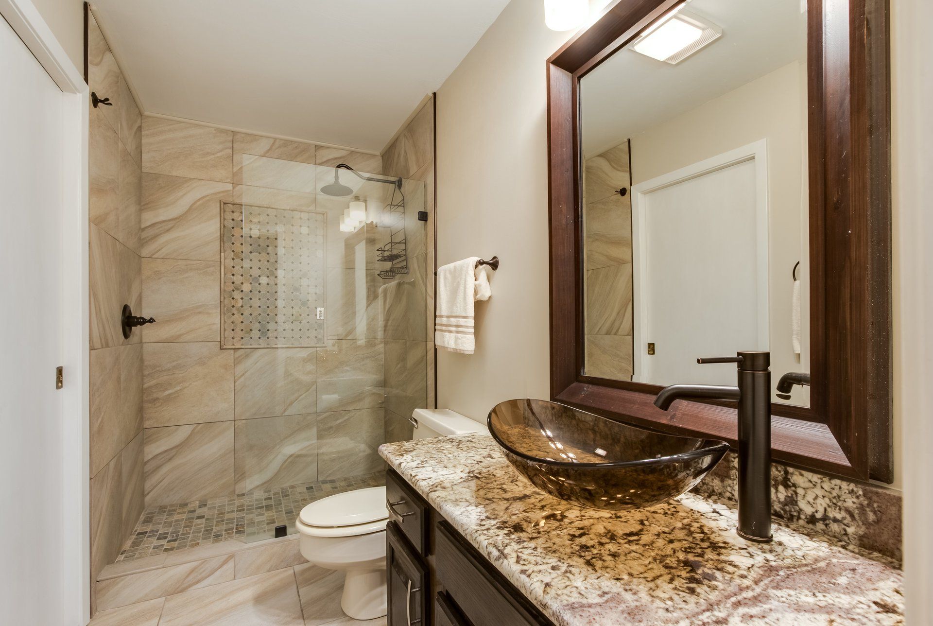 A bathroom with a toilet , sink , mirror and walk in shower.