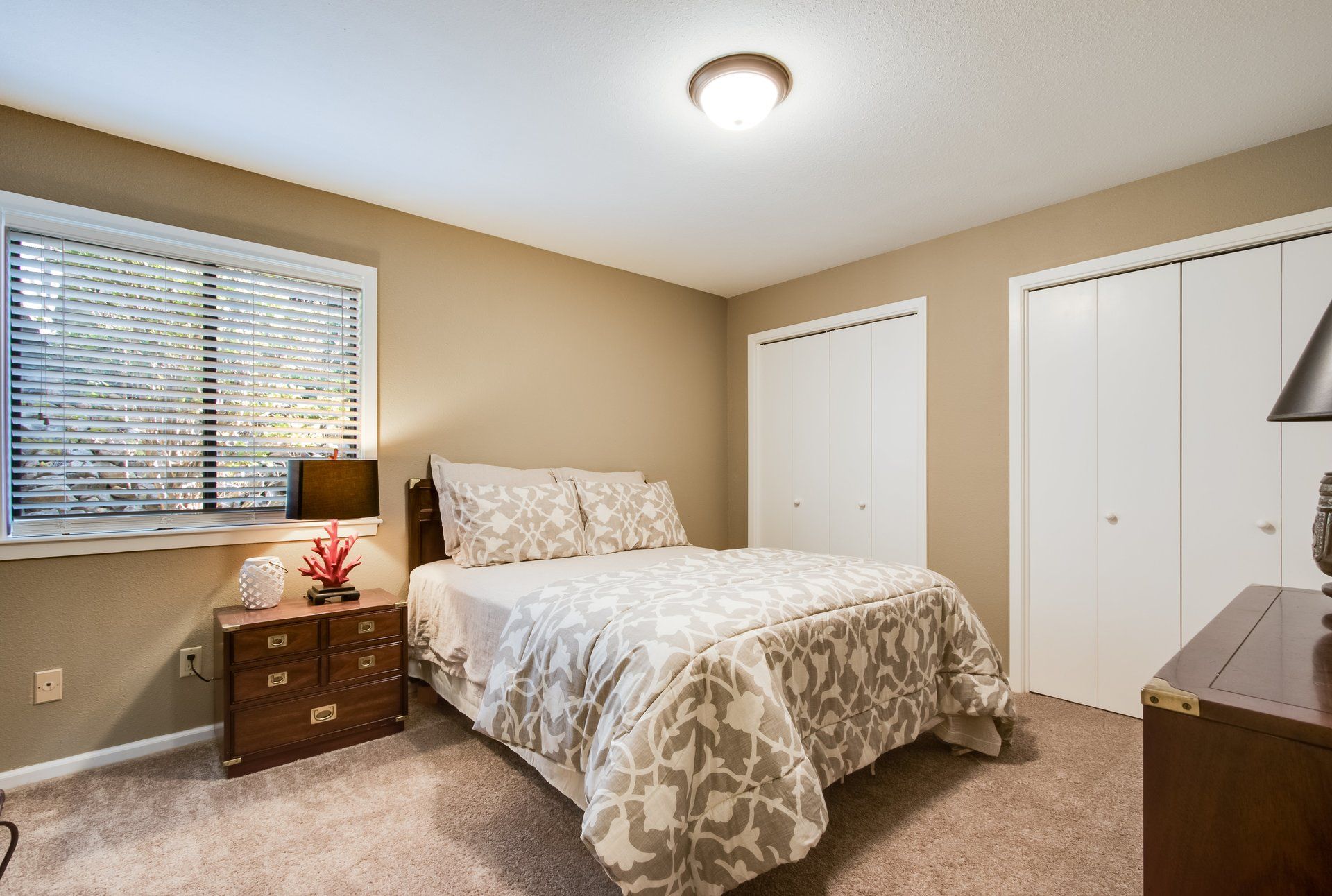 A bedroom with a bed , nightstand , lamp and window.