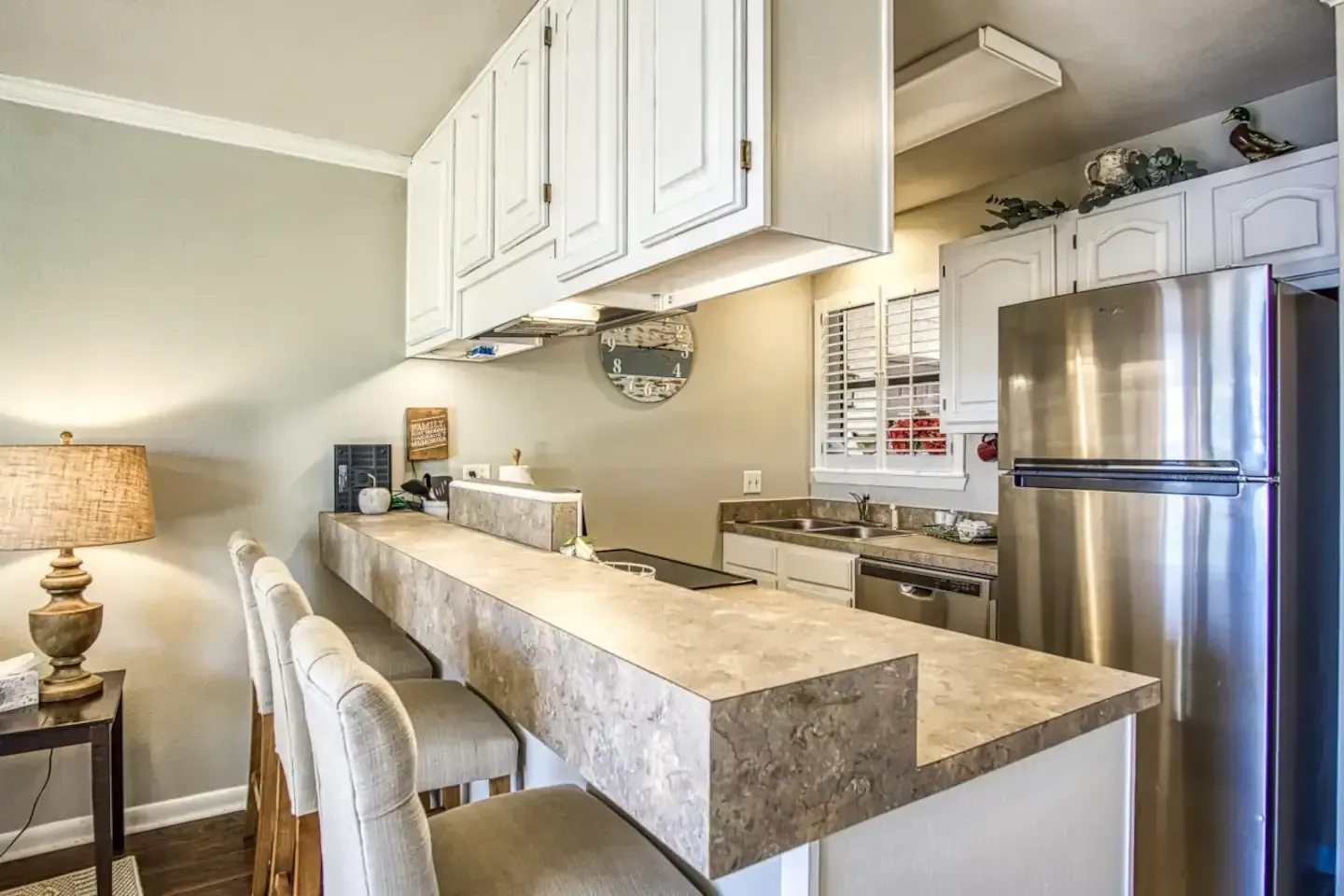 A kitchen with a long counter and stools and a refrigerator.