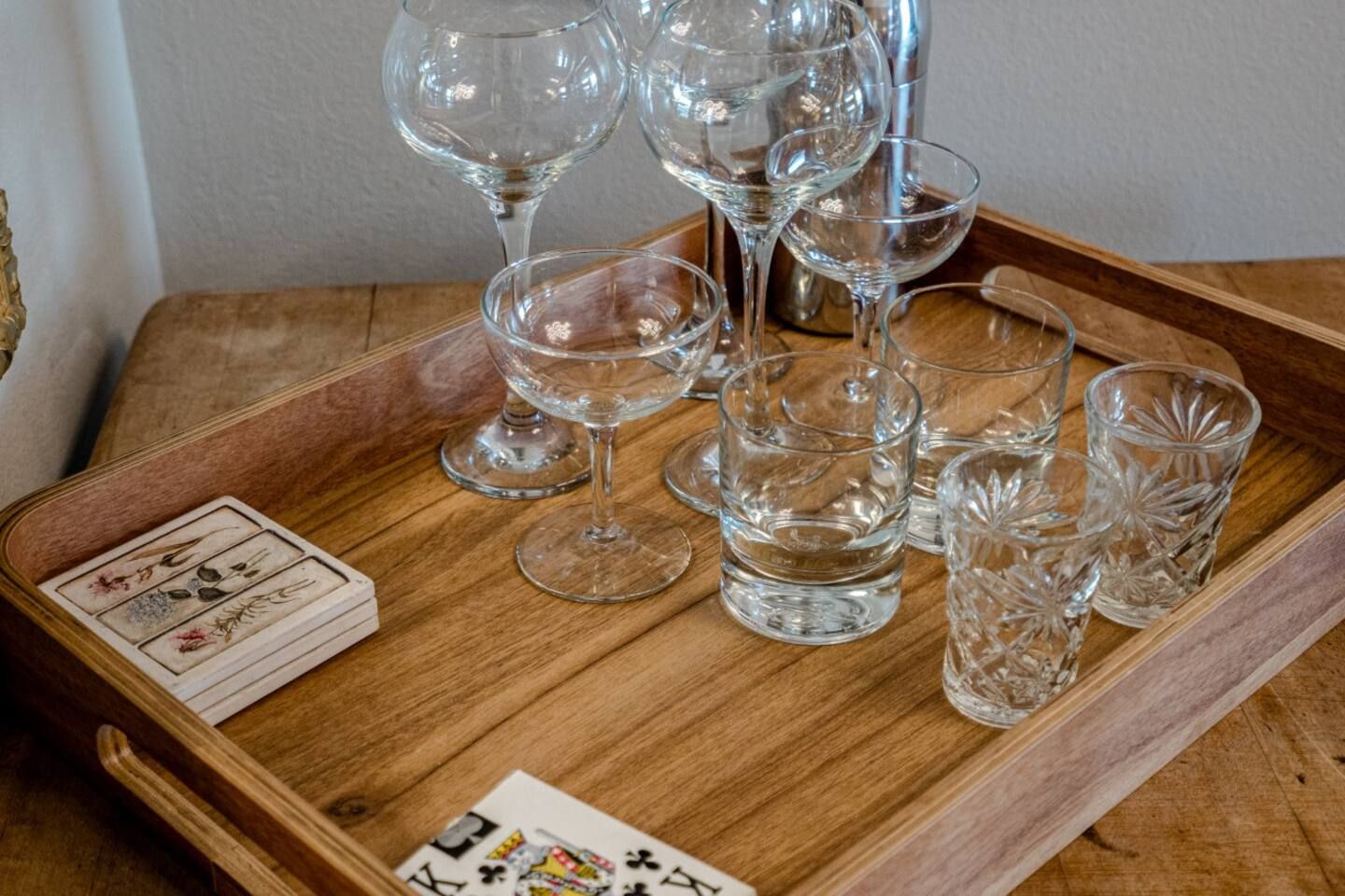 A wooden tray with wine glasses , shot glasses , and playing cards on it.
