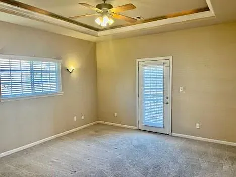 An empty living room with a ceiling fan and a sliding glass door.
