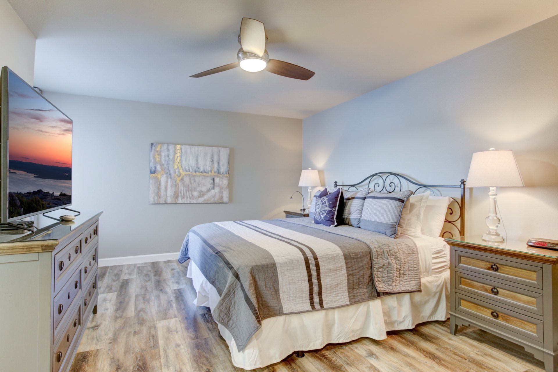 A bedroom with a king size bed , dresser , nightstand , television and ceiling fan.