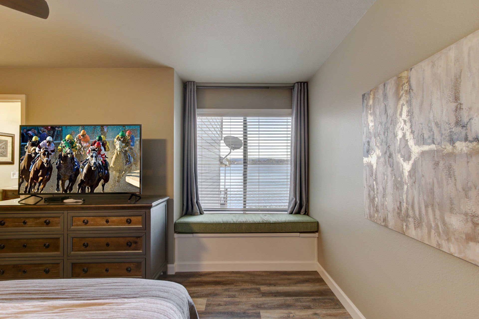 A bedroom with a bed , dresser , television and window seat.