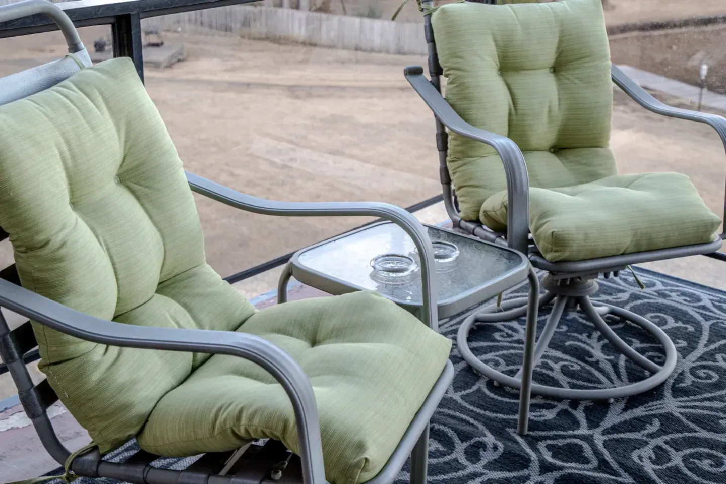Two chairs and a table on a patio with green cushions.