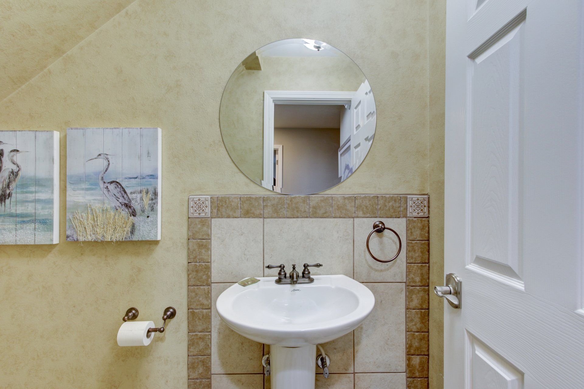A bathroom with a pedestal sink and a round mirror