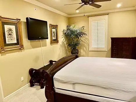 A bedroom with a bed , dresser , television and ceiling fan.