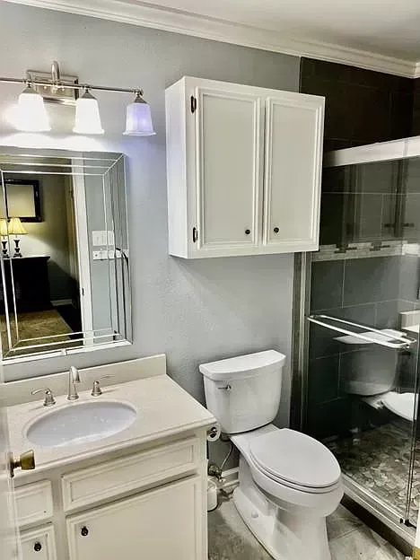 A bathroom with a toilet , sink , mirror and walk in shower.