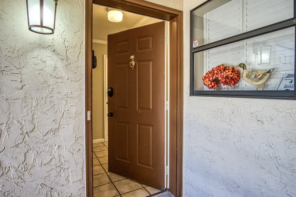 A brown door is open to a white wall with a window.