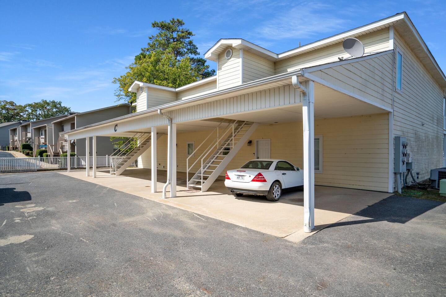 A white car is parked under a carport in front of a building.