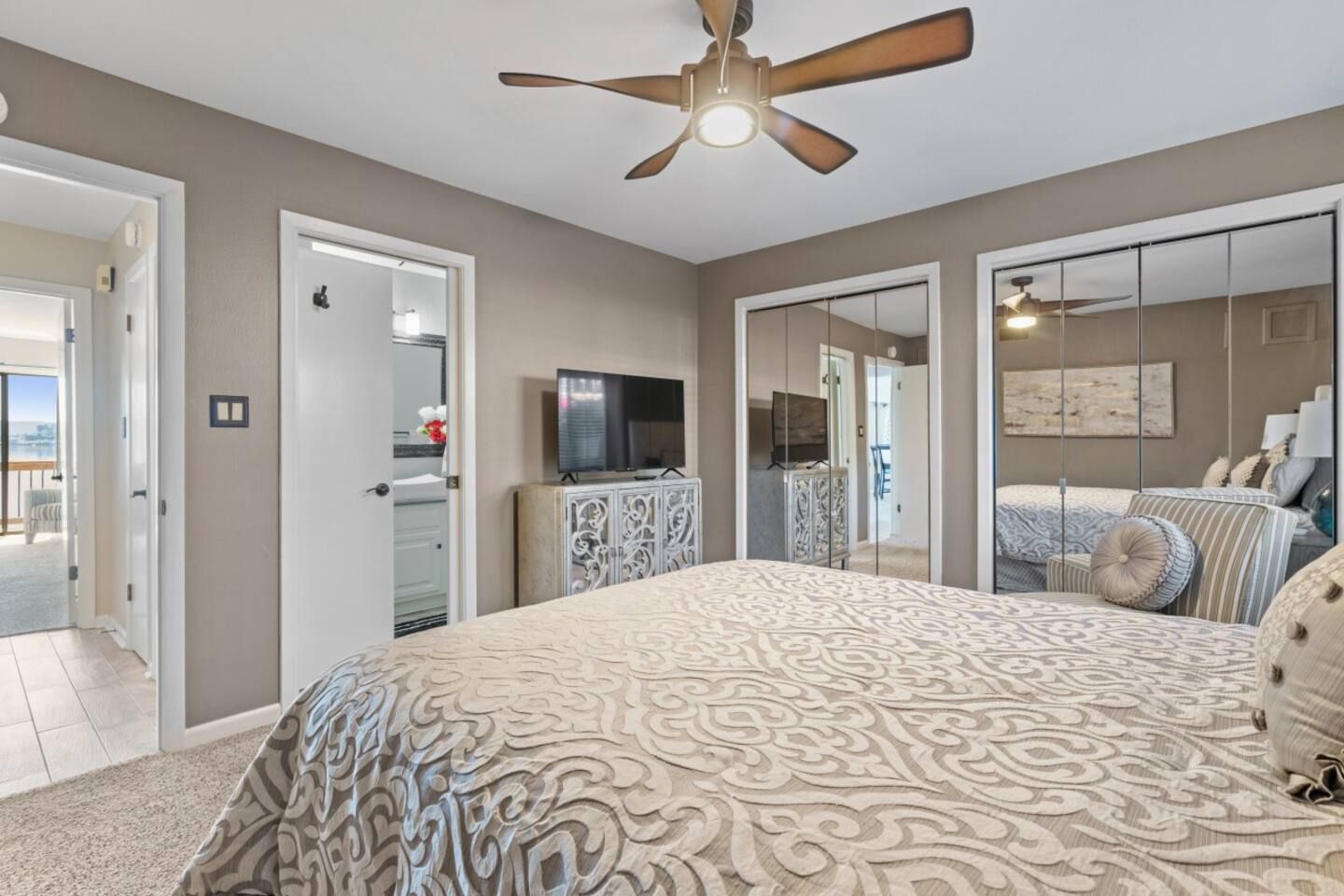 A bedroom with a king size bed , ceiling fan , television and mirrored closets.