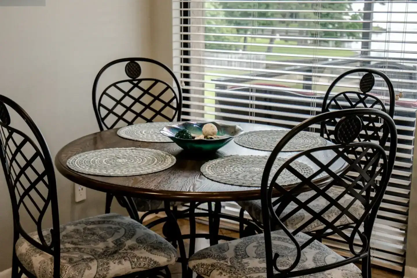 A dining room table and chairs in front of a window with blinds.