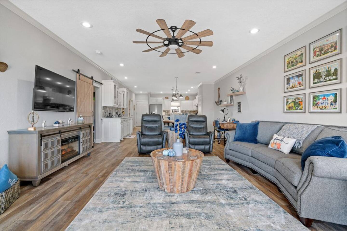 A living room with a couch , chairs , coffee table , television and ceiling fan.