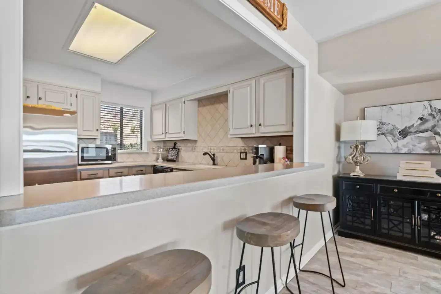 A kitchen with stools and a window looking into the kitchen.