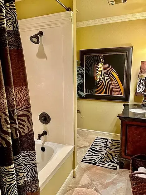A bathroom with a zebra print shower curtain and a picture of a zebra on the wall.