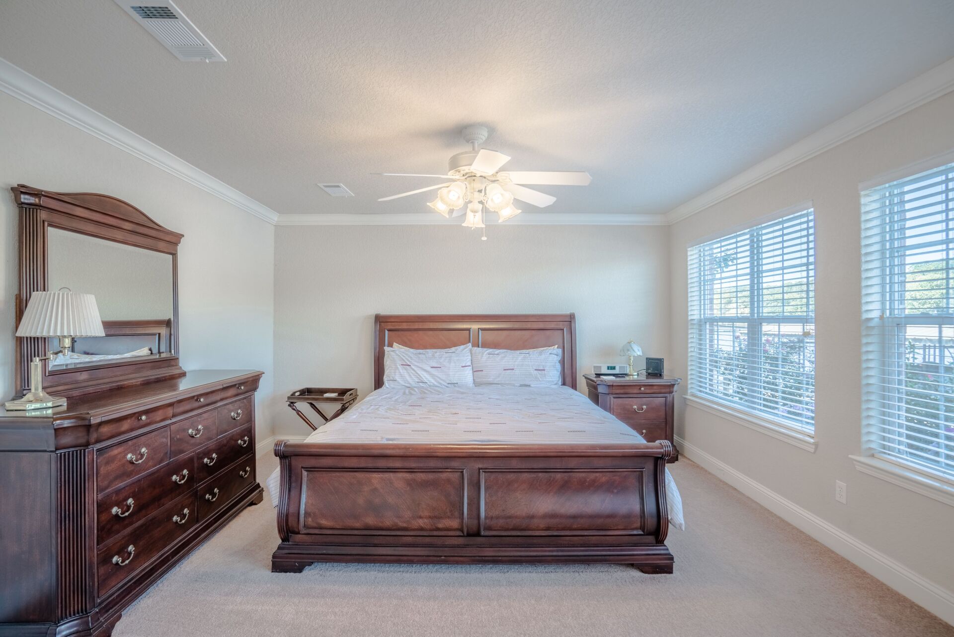 A bedroom with a king size bed , dresser , mirror and ceiling fan.