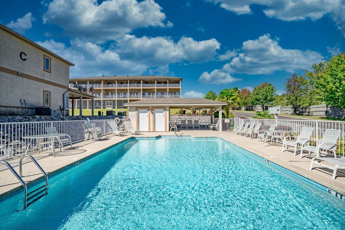 A large swimming pool surrounded by chairs and tables in front of a building.