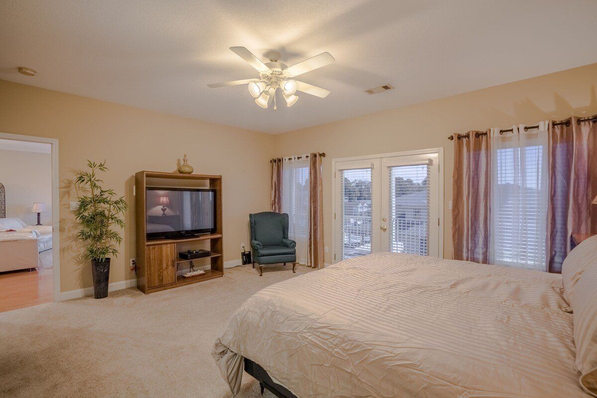 A bedroom with a king size bed , television , chair and ceiling fan.