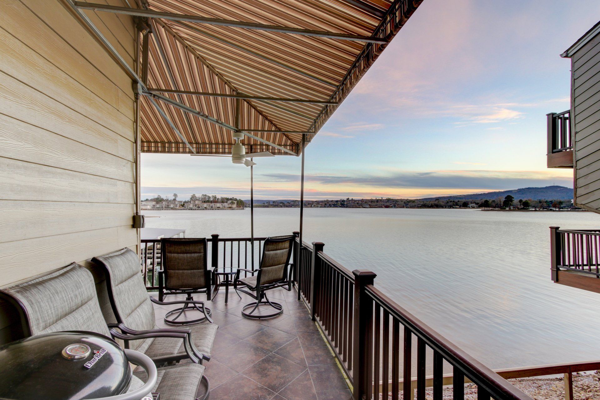 A balcony with a grill and chairs overlooking a body of water.